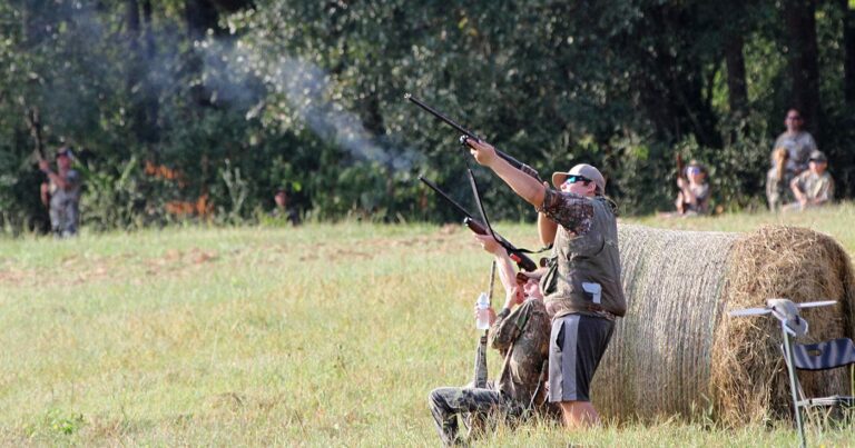 Two dove hunters positioned in a field next to a hay bale.