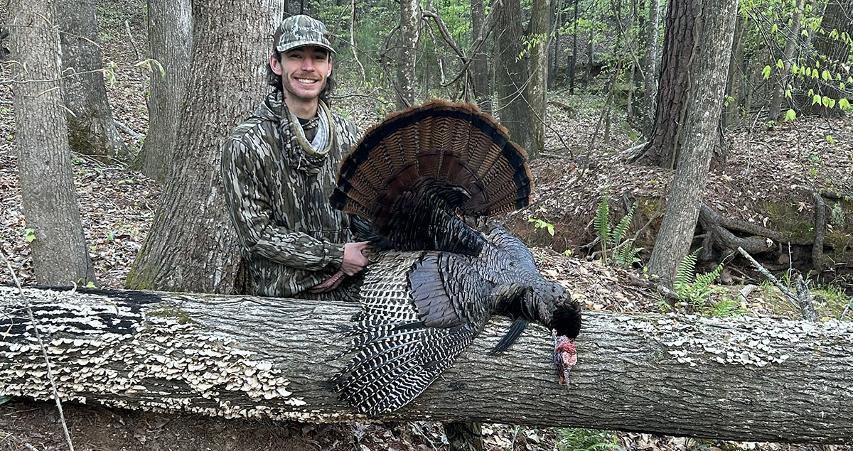 A hunter with a turkey laying on a log.